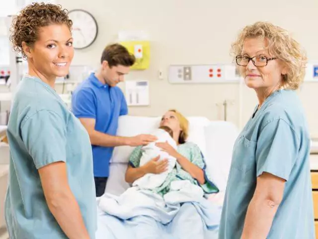 widwives looking at camera in front of couple with newborn baby